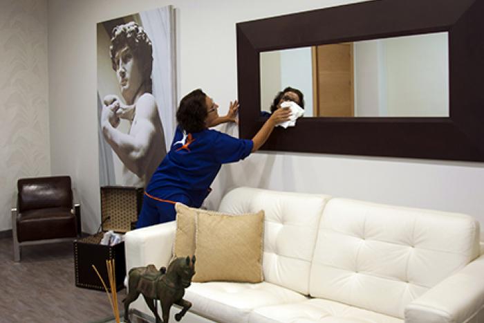 Un employé du Groupe SIFU nettoie un miroir dans une chambre d'hôtel